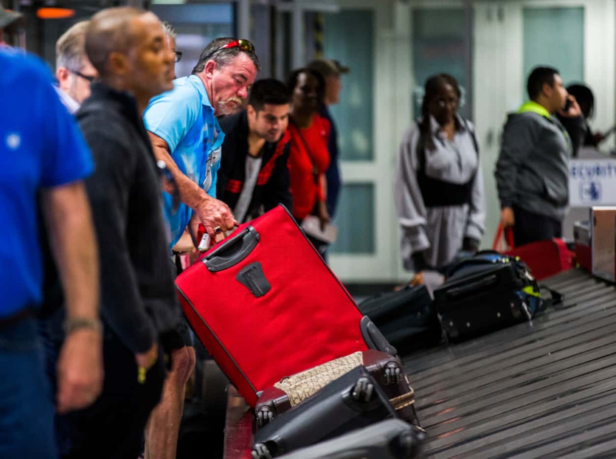 A traveler retrieves his bag as luggage moves around a baggage claim at Gate C on Friday,...
