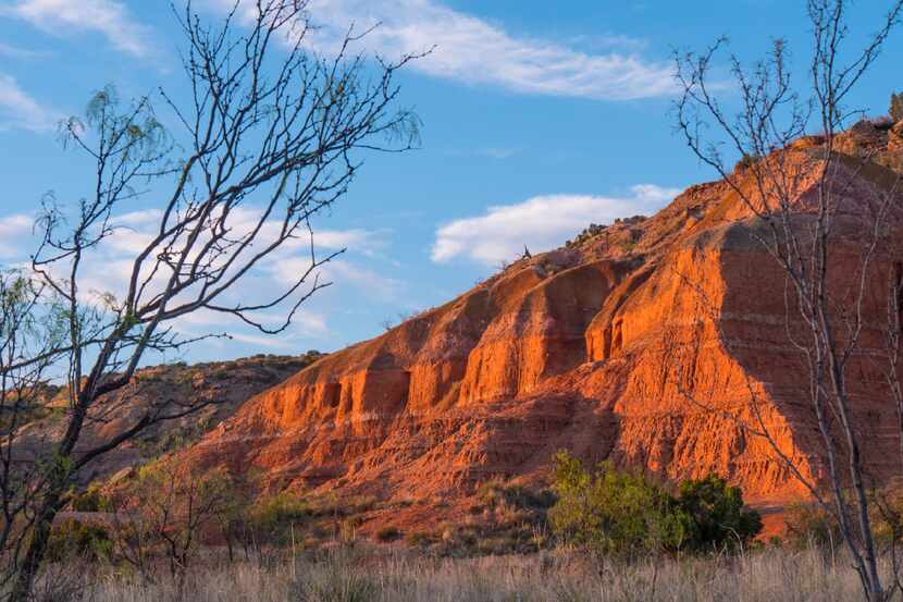 The ruddy walls of Palo Duro Canyon State Park blush in the light of the setting sun.  Folks...