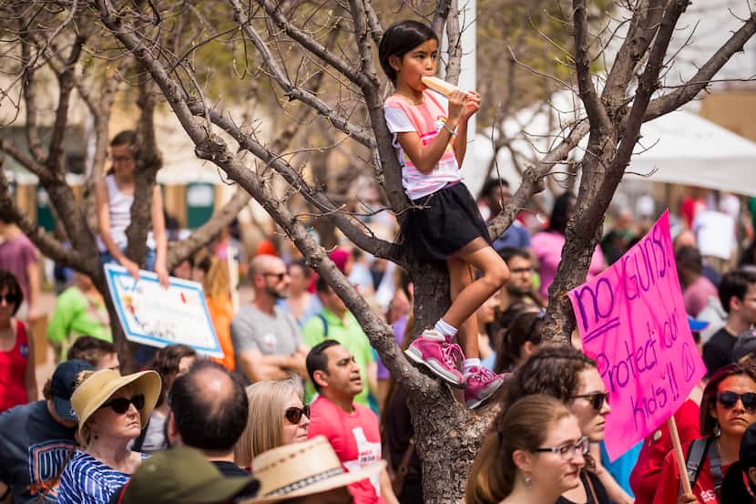 Isabelle Garcia-Chu, 8, of Richardson, stands in a tree while eating a popsicle and...