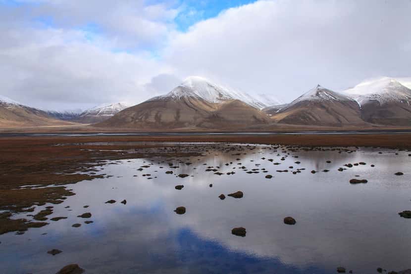 Perennially ice-capped mountains are reflected in pools in the tundra near Longyearbyen,...