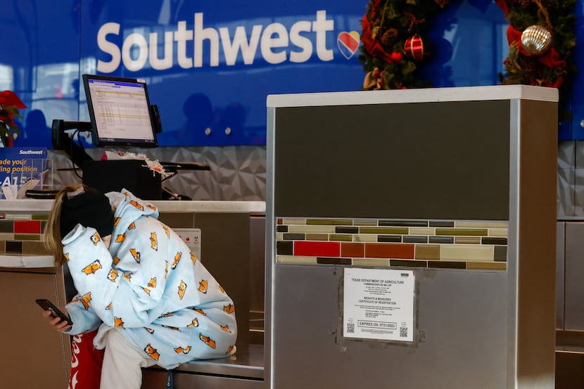 A traveler watches her phone while waiting for a Southwest Airlines agent to return to the...