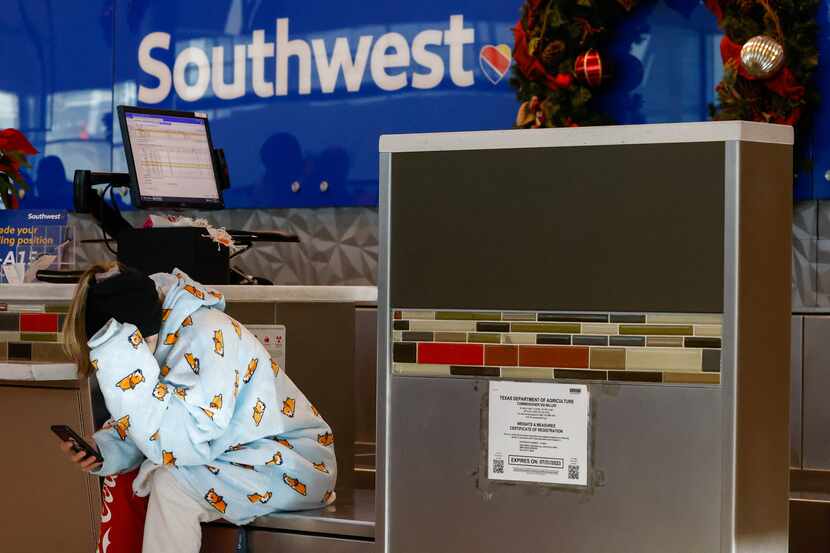 A travelers sits on their phone as they wait for a Southwest Airlines agent to return to the...
