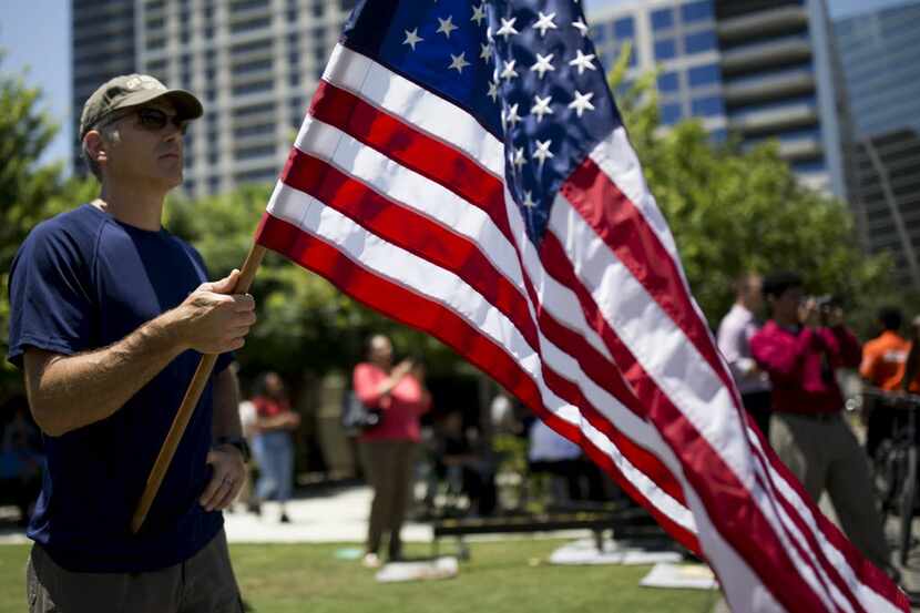 Rod Baird, of Dallas, holds a U.S. Flag while standing in the park watching the live...