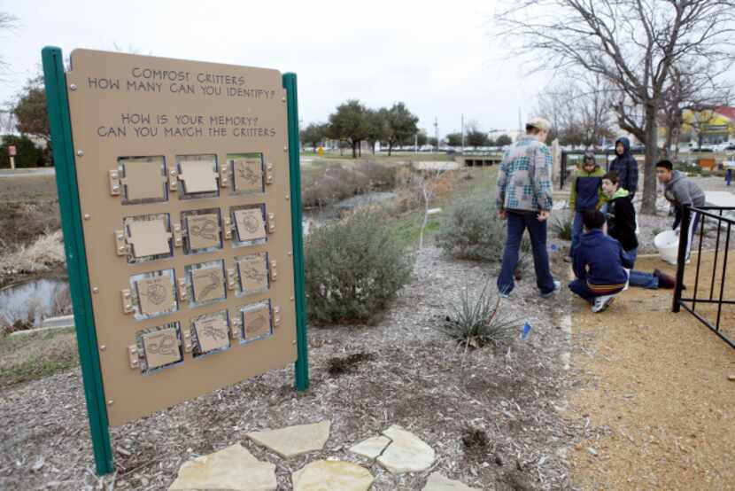 Volunteers pull weeds near a sign about compost critters at Plano Environmental Education...