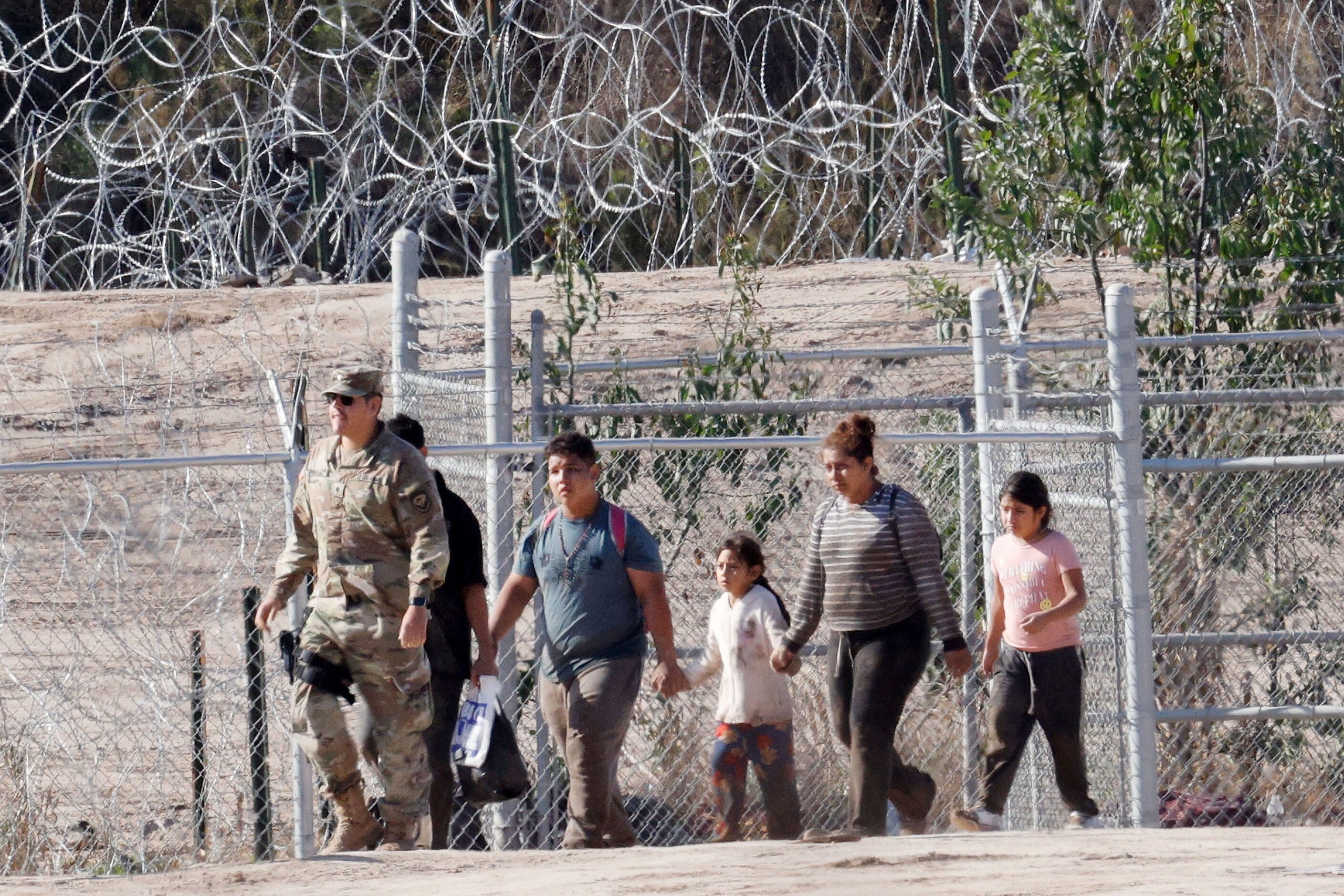 Migrants are escorted by an U.S. soldier with the 508th Military Police Company from New...