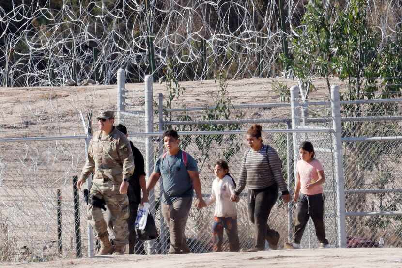 Migrantes son escoltados por soldados de Estados Unidos hacvia un punto de control...