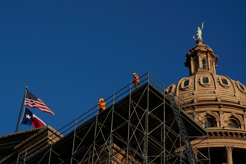Construction workers look out from scaffolding for a roof restoration project as the Texas...