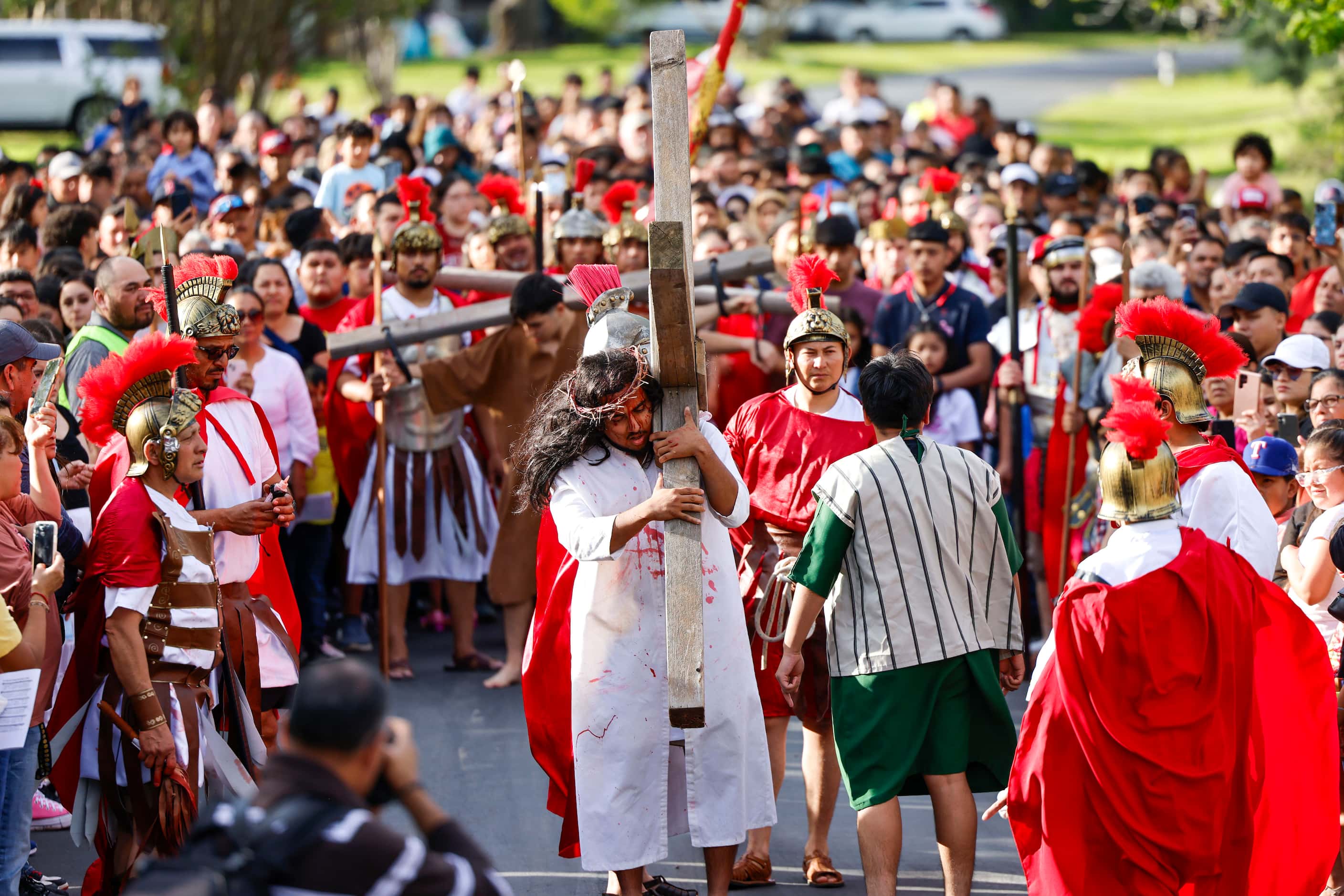 Crowd follows as Bernie Gonzalez carries the cross during Living Stations of the Cross...