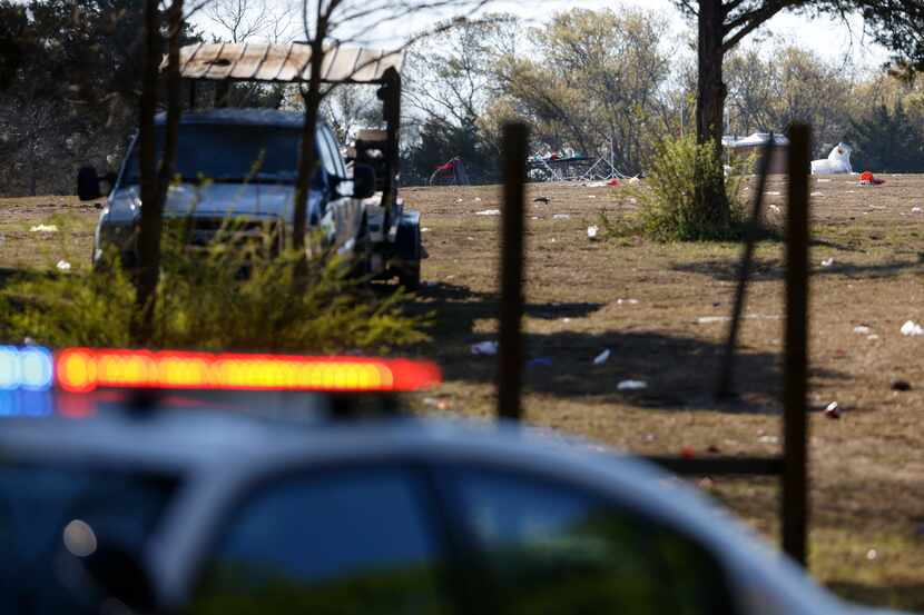A police car sits Sunday in front of the field where a person was killed and 16 others were...