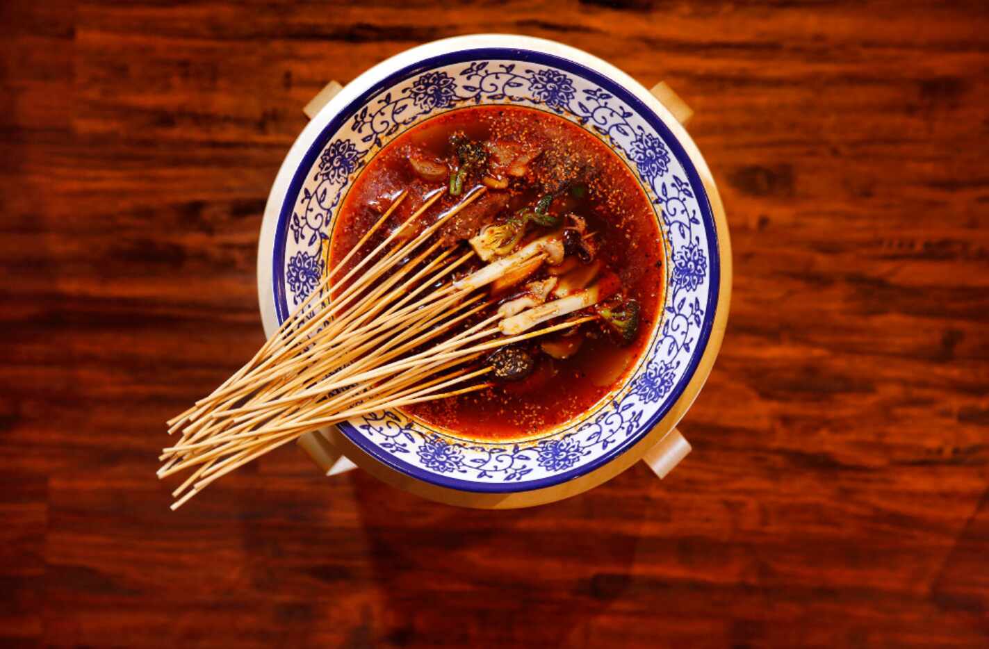 Skewers in large simmering bowl of medium, spicy chicken broth with Sichuan peppers is...