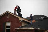Roofers look to cover a house damaged by a Tornado in Southwest Arlington, Texas near...