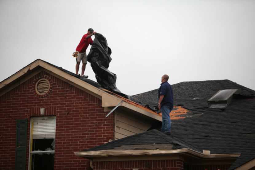 Roofers look to cover a house damaged by a Tornado in Southwest Arlington, Texas near...