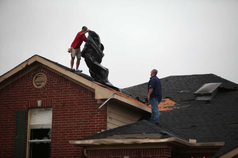 Roofers looked to cover a house damaged by a tornado in southwest Arlington near Kennedale...