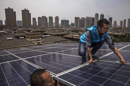 Chinese workers from Wuhan Guangsheng Photovoltaic Company install solar panels on the roof...