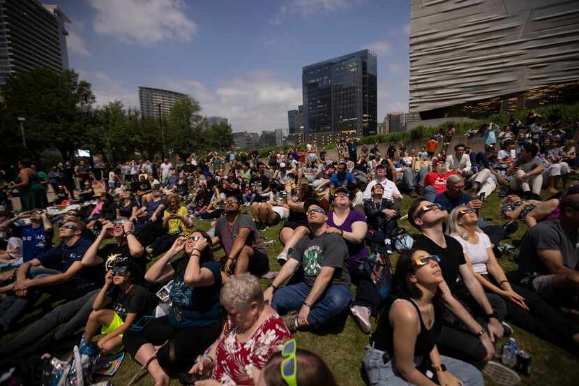People watch the eclipse near totality as building lights turn on behind them during the...