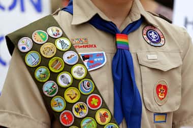 Merit badges and a rainbow-colored neckerchief slider are affixed on a Boy Scout uniform in...