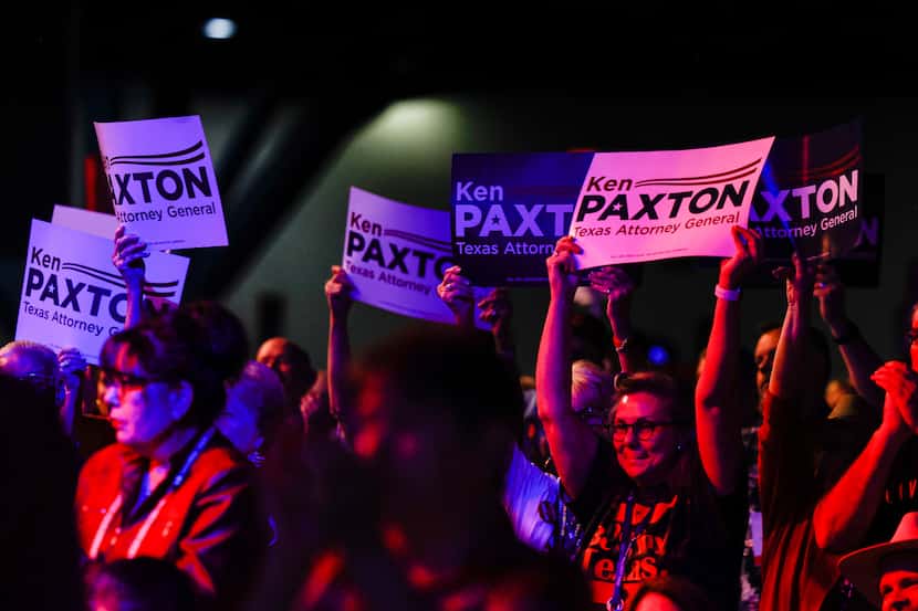 Attendees show Ken Paxton's signs as he gives a speech during a general meeting as part of...
