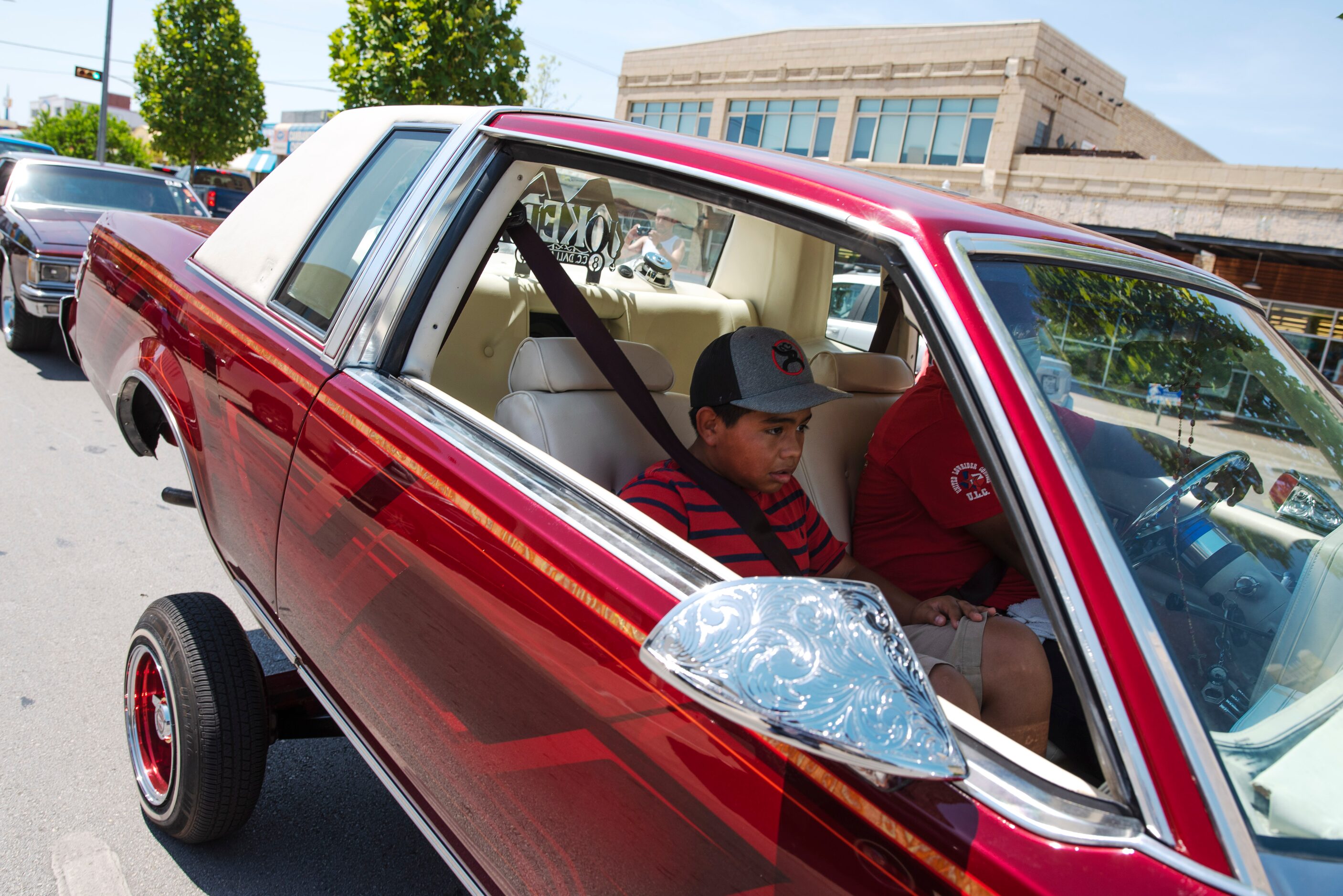 A young boy rides inside a classic car as lowriders from the United Lowriders Association...