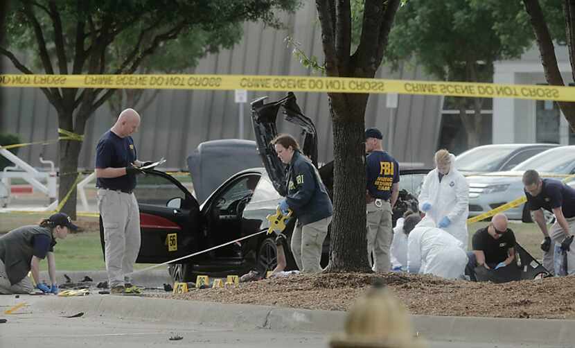 FBI agents collect evidence around the car driven by two men killed Sunday when they opened...