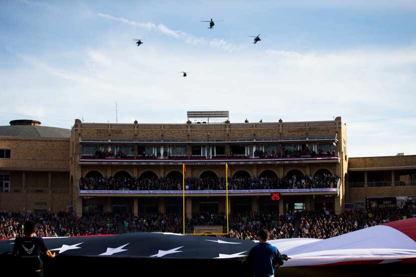 Military helicopters fly over a large American flag before the Armed Forces Bowl between the...