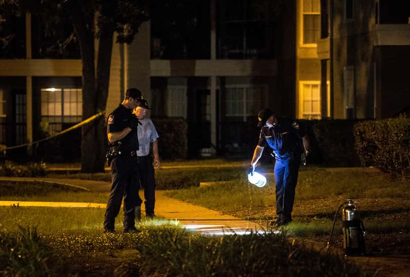 Lewisville police officers clean bloodstains from the pavement at Oak Forest Apartments in...