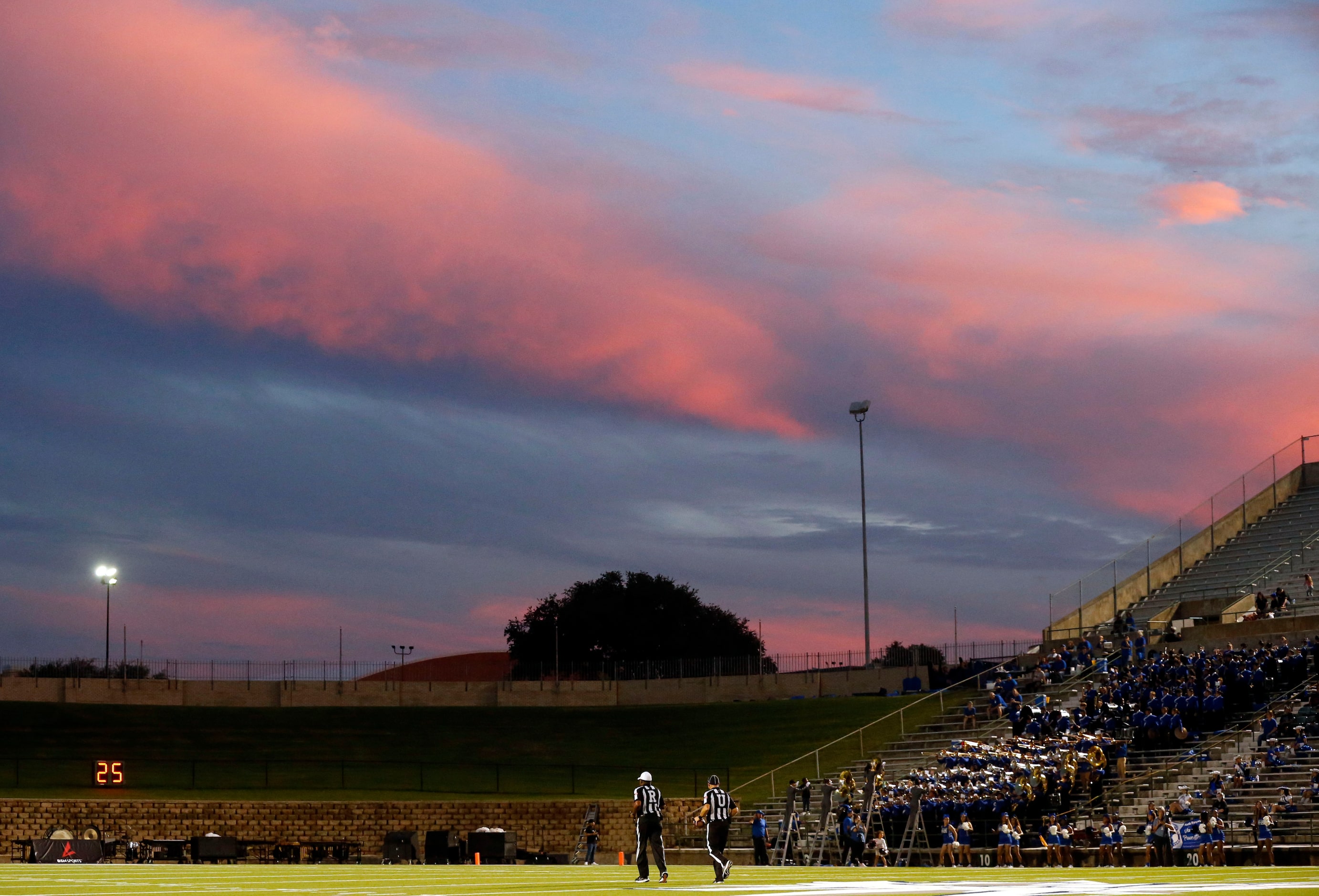 Officials walk toward the other end of the field, as the dusk is reflected onto waning storm...