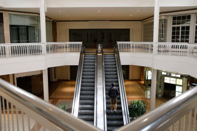 A man rides an escalator toward an empty storefront that used to be a Macy's at Collin Creek...