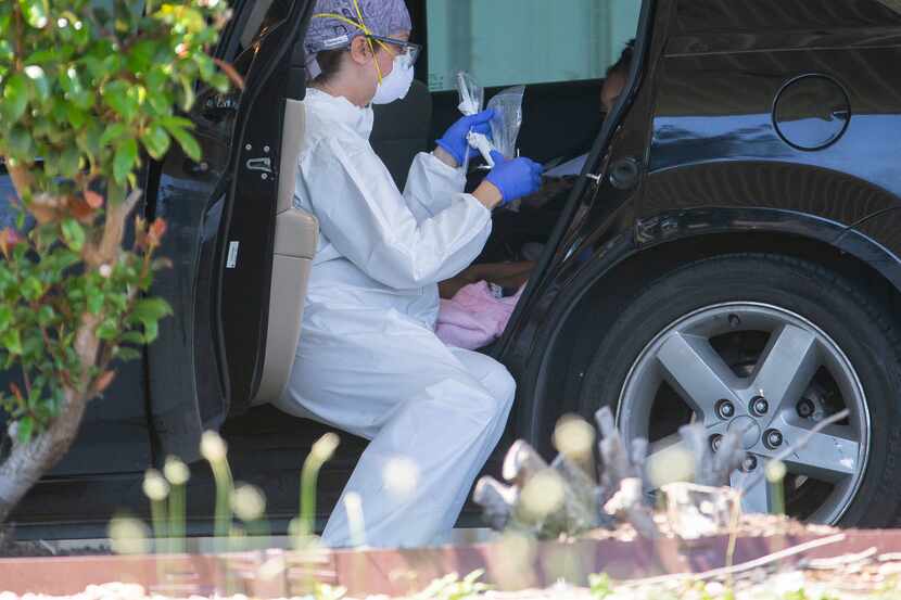 A healthcare worker for MD Medical Group tests a child for COVID-19 in the backseat of a car...