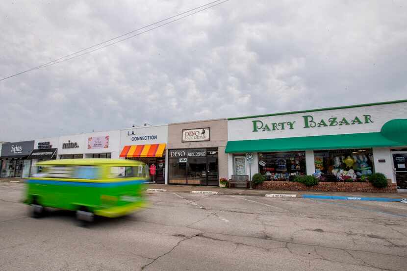 A brightly painted Volkswagen bus drives past shuttered small businesses near Lovers Lane...