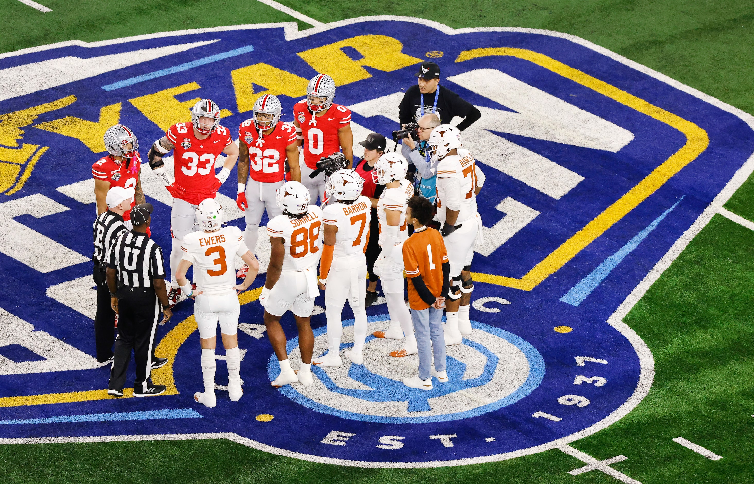 The Texas Longhorns and Ohio State Buckeyes captains watch the coin toss before a CFP...