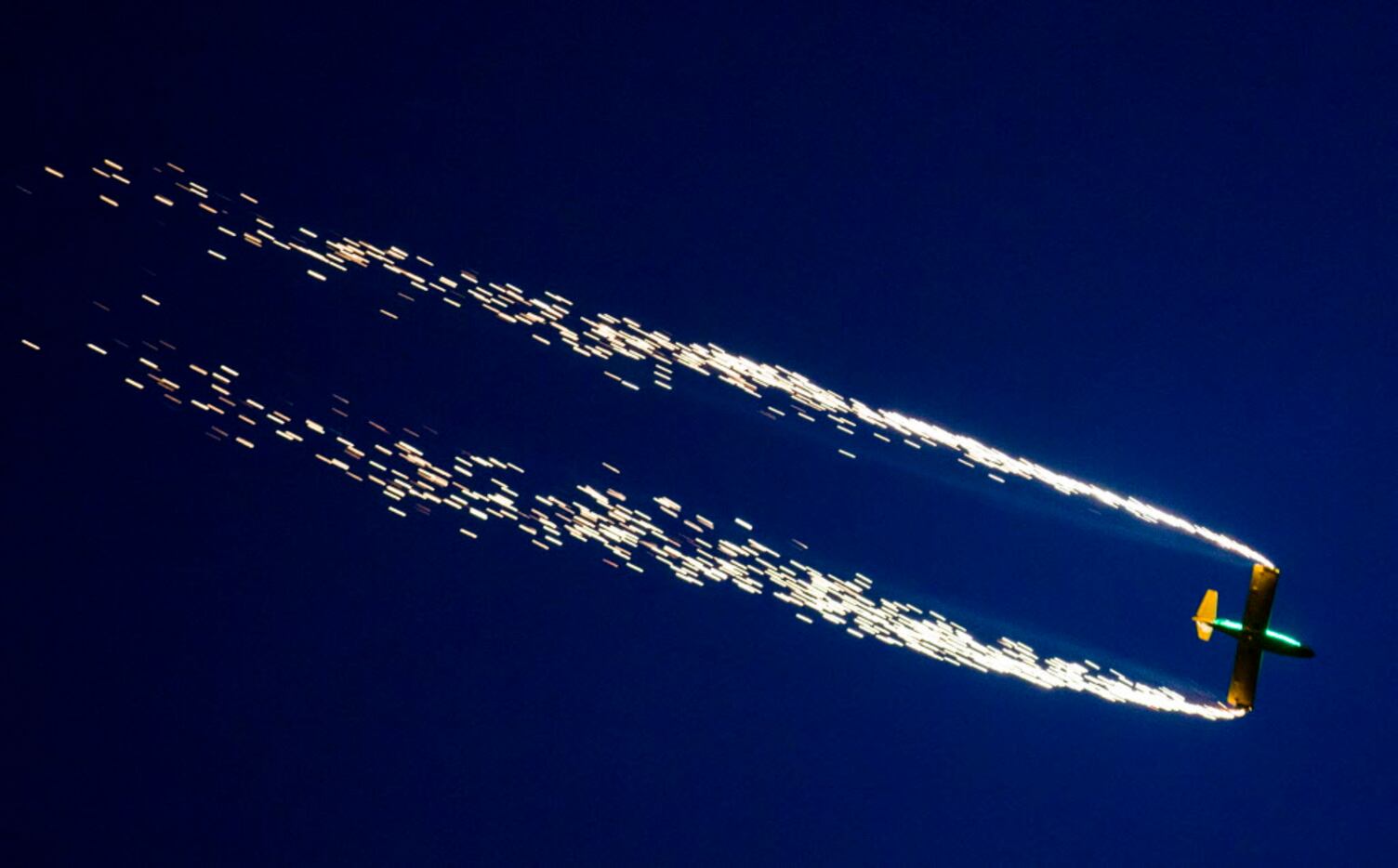 An airplane trails sparks as part of an airshow during the Addison Kaboom Town! festival and...