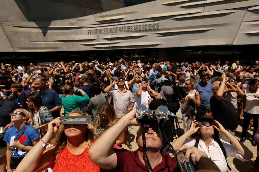 People watch the sun during a solar eclipse outdoor watch party at the Perot Museum of...