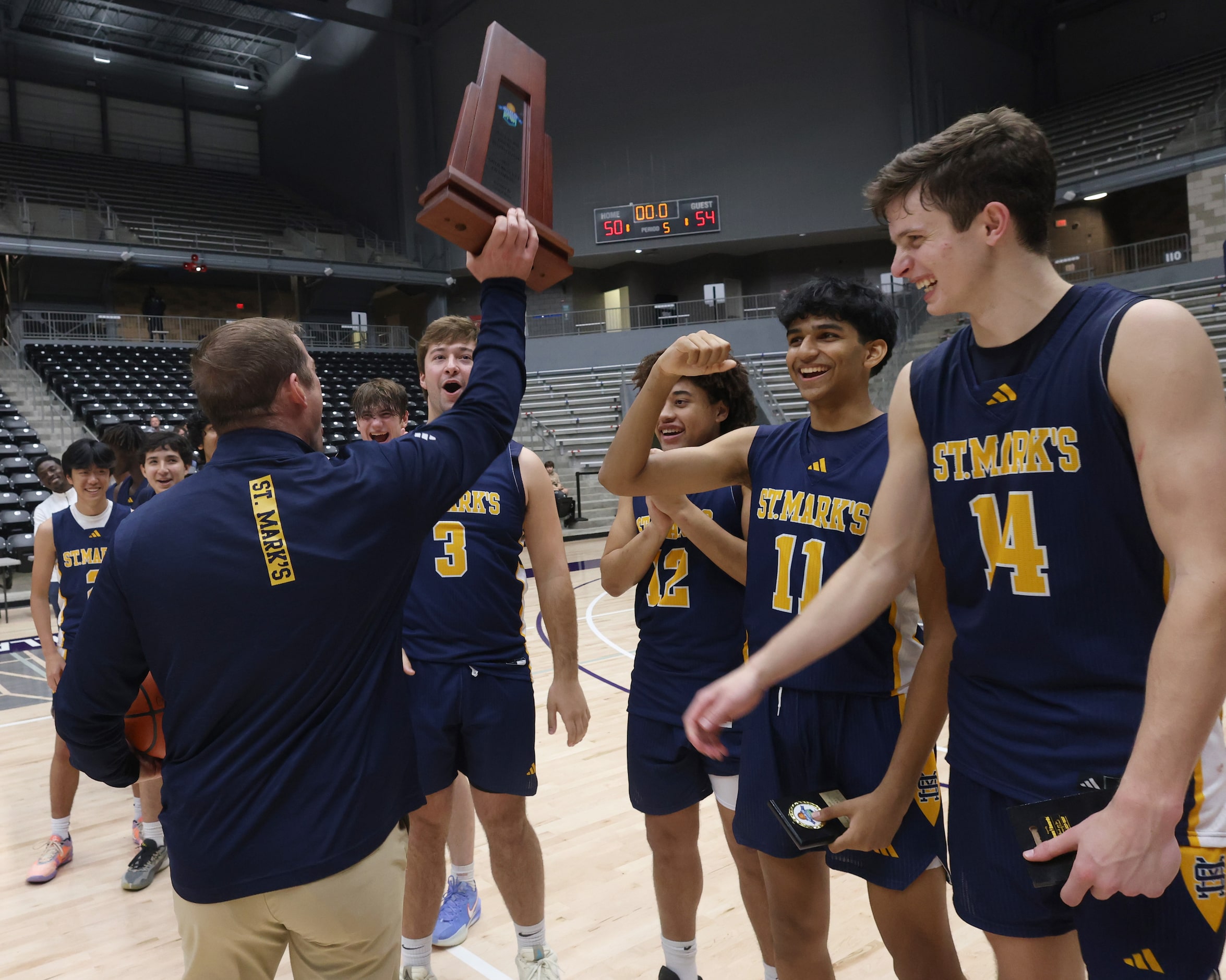 St. Mark's head coach Greg Guiler, left, hoists the tournament championship trophy after his...