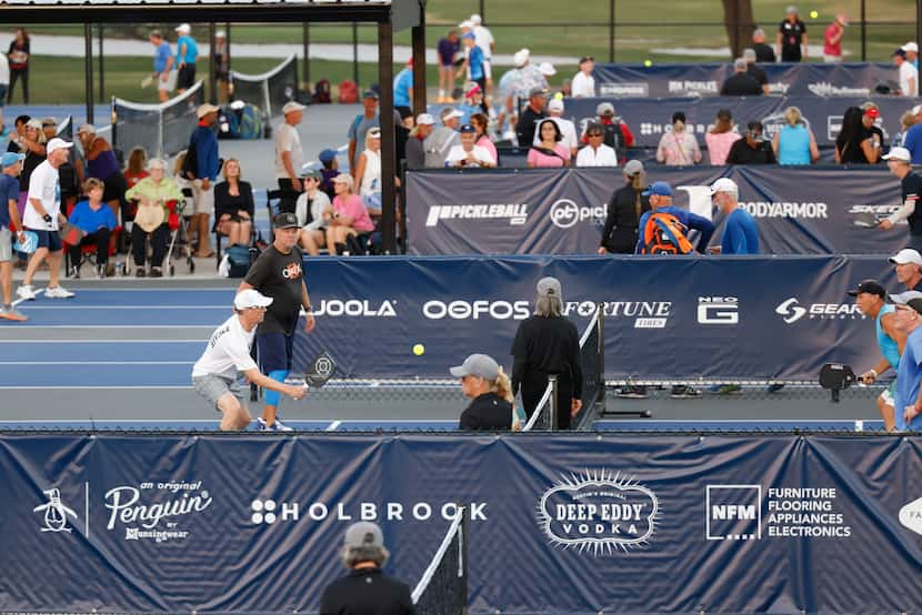 Corporate sponsor names line the fencing separating courts at Brookhaven Country Club in...