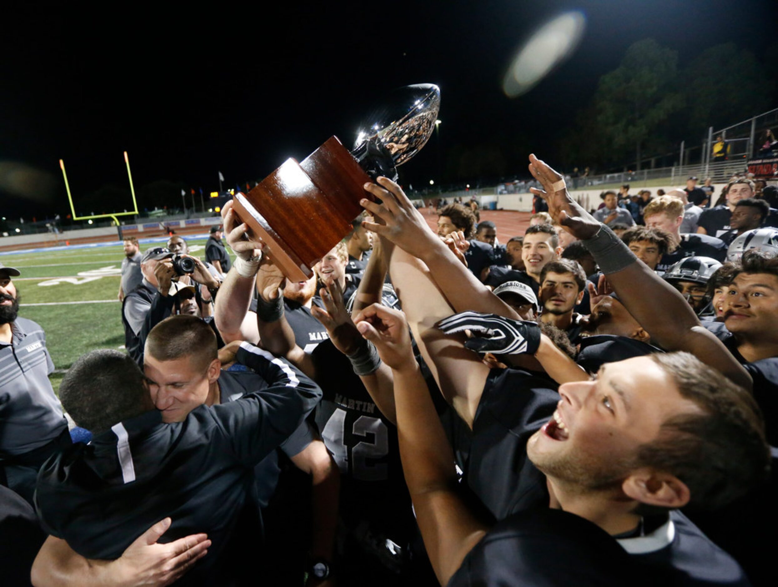 Arlington Martin Players and coach Bob Wager (bottom left) react to their playoff trophy...