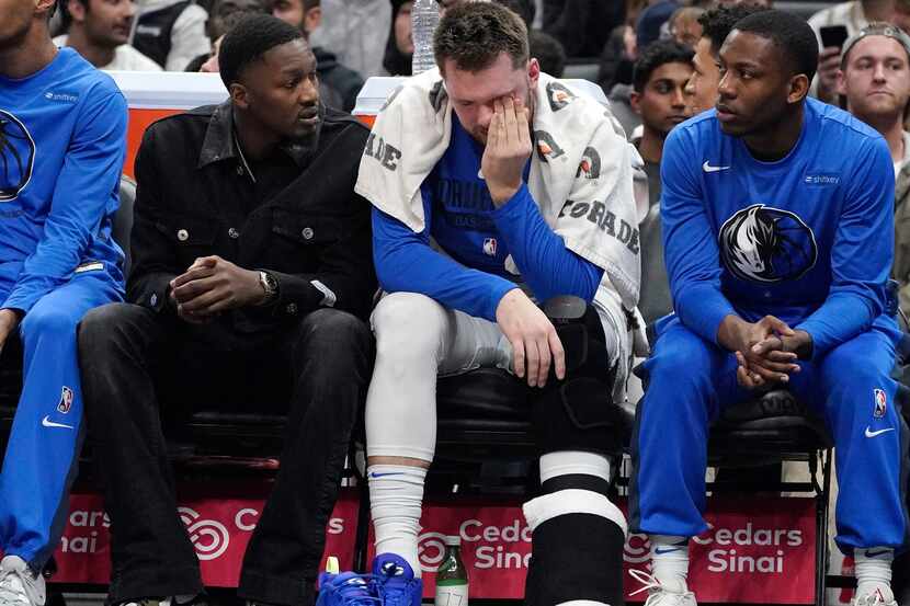 Dallas Mavericks guard Luka Doncic, center, sits on the bench during the first half of an...