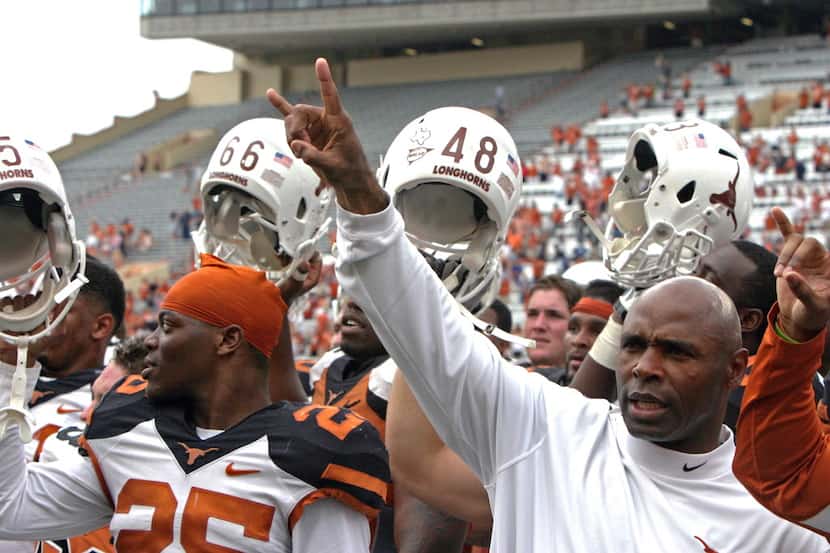 Texas coach Charlie Strong gives the "hook 'em horns" sign while his players raise their...