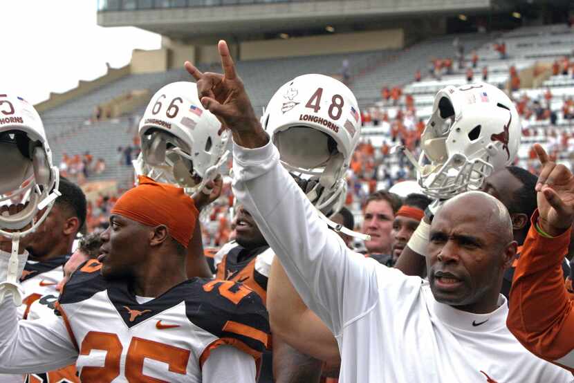 Texas coach Charlie Strong gives the "hook 'em horns" sign while his players raise their...