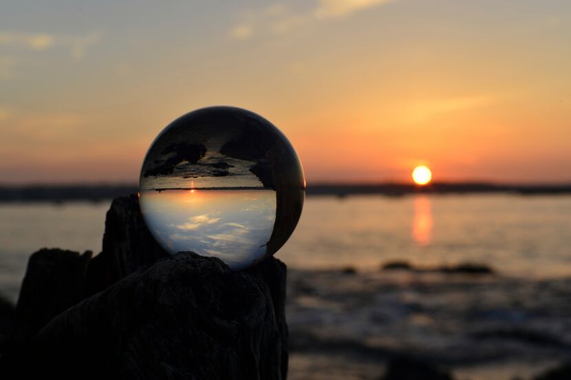 Glass sphere balanced on a stump by the beach at sunrise.