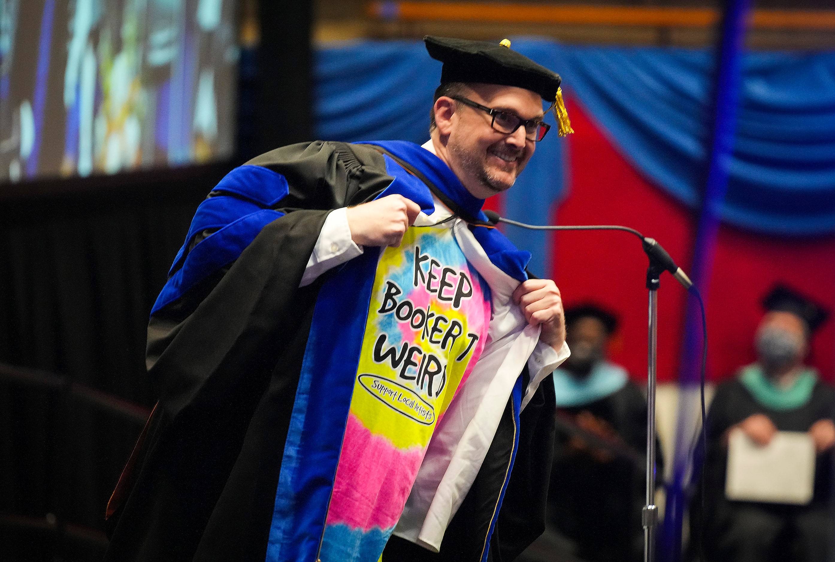 Principal Scott Rudes rips open his cap and gown to show off  a “Keep Booker T Wierd”...