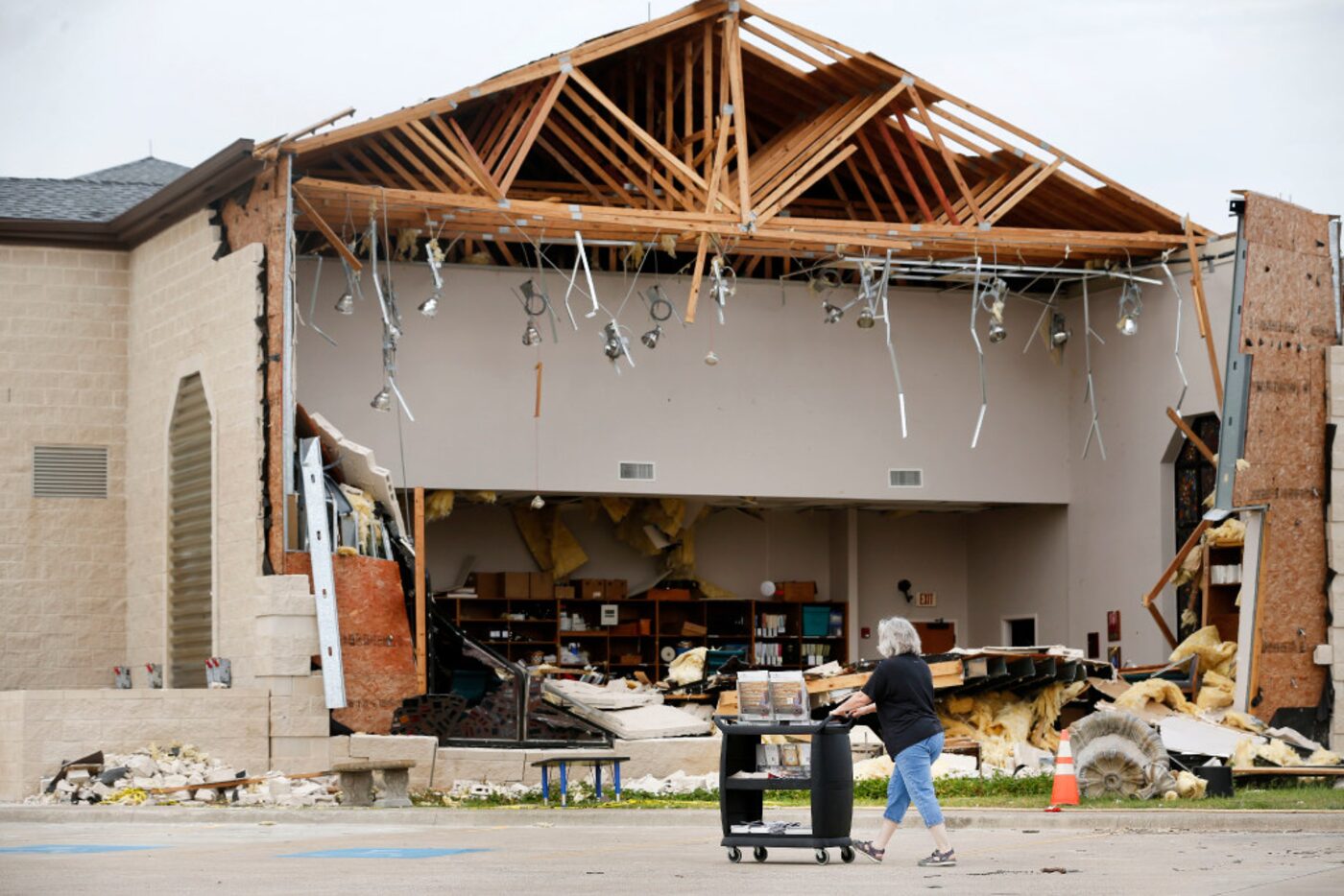 Patty Albin pushes a cart of daily devotionals past the damaged sanctuary at First Baptist...