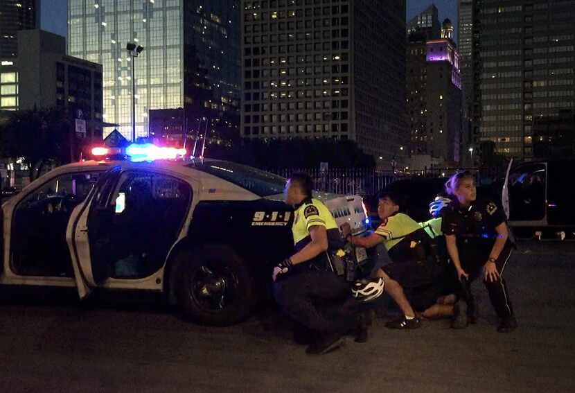 Dallas Police officers take cover behind a police cruiser as shots are fired following a...