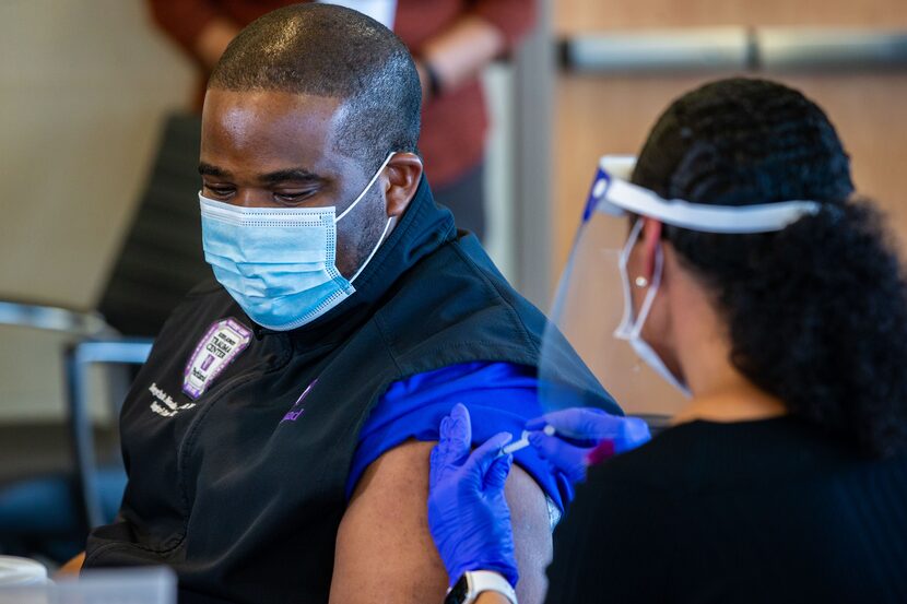 COVID unit nurse Tonychris “TC” Nnaka, (left) receives a dose of the Pfizer COVID-19...