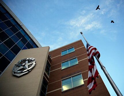 Birds fly by a flag at half mast in front of Dallas Police Department headquarters Friday,...