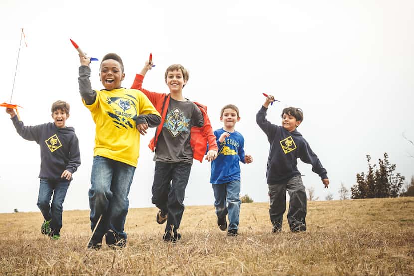 A group of young scouts runs through a field with toy rockets.