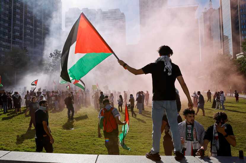 A man waves a Palestinian flag as colored smoke bombs fill the air during a protest...