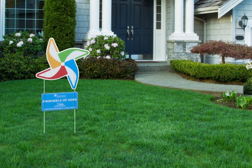 A yard sign in the shape of a pinwheel, in the middle of a green lawn with a house in the...