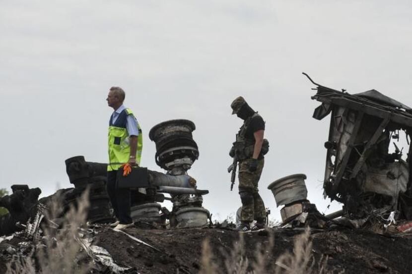 
A Ukrainian investigator, left,walks by charred debris as a pro-Russian fighter guards him,...