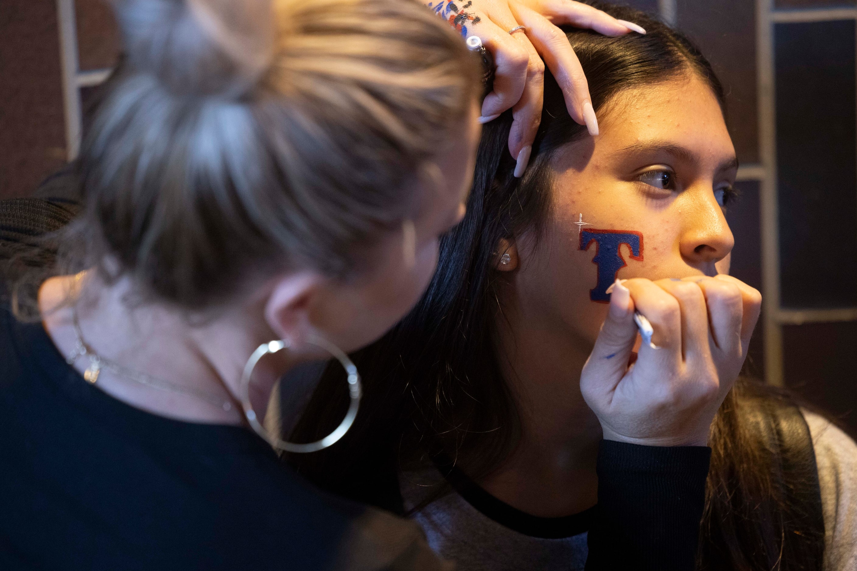 Heidi Lara of Fort Worth paints a Texas Rangers “T” on Rachel Martinez, 13, of Grand Prairie...