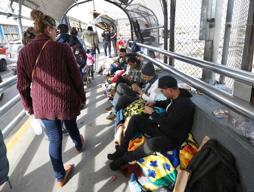 Documented border crossers walk past a group of undocumented migrants waiting to enter the...